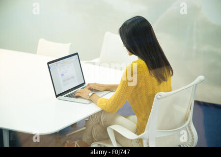 Vue arrière portrait of a brunette businesswoman working on laptop in office Banque D'Images