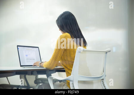 Vue arrière portrait of a casual businesswoman working on laptop in office Banque D'Images