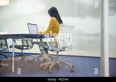 Vue arrière portrait of a casual businesswoman working on laptop in office Banque D'Images