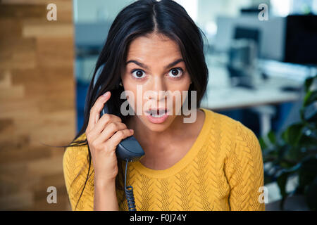 Portrait d'un surpris businesswoman talking on the phone in office Banque D'Images
