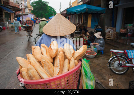 Chapeau de femme Vietnam, vue arrière d'une femme portant un chapeau conique transportant du pain au marché de Hoi an, Centre du Vietnam. Banque D'Images