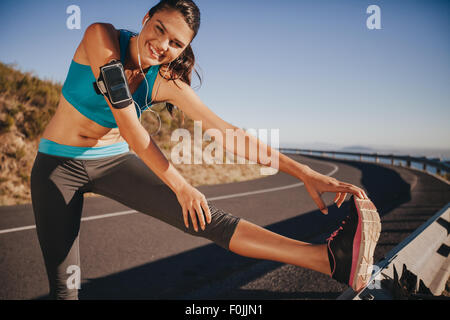 Athlète féminin s'étend ses jambes avant d'exécuter en plein air. Jeune femme fit l'échauffement pour une course sur route de campagne. Banque D'Images
