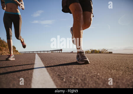 Cropped shot of a young athletes running à l'extérieur. Un pays pour les coureurs sur route matin d'été. L'homme et la femme le jogging sur Banque D'Images