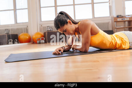 Femme de remise en forme situé sur tapis d'exercice à la recherche à son téléphone mobile. Femme à l'aide de smart phone après sa séance d'entraînement à la salle de sport. Banque D'Images