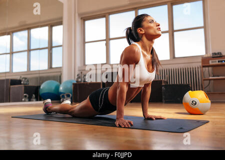 Femme extensible de base sur Tapis de fitness. La jeune femme qui s'étend de l'exercice dans la salle de sport. Banque D'Images