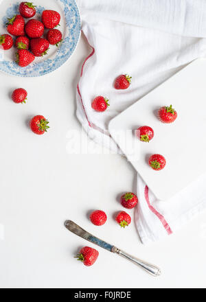 Les fraises dans une assiette blanche et bleue et sur la table et planche à découper Banque D'Images