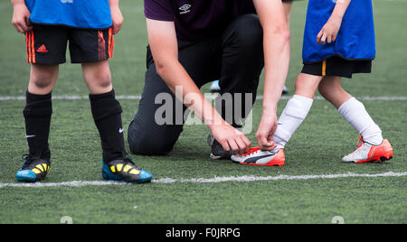 Professeur de sport attache les lacets d'un jeune enfant au cours d'un match de football.