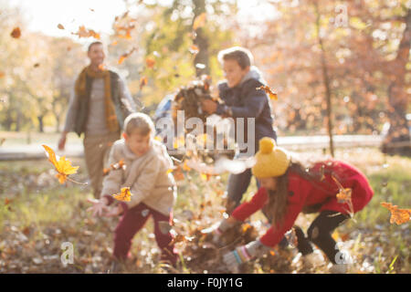 Famille jouant dans les feuilles d'automne au parc Banque D'Images