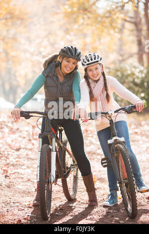 Portrait of smiling mother and daughter on mountain bikes in woods Banque D'Images