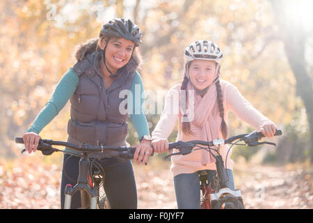 Portrait of smiling mother and daughter on mountain bikes in woods Banque D'Images