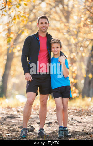 Portrait of smiling father and son in sportswear sur le chemin dans les bois Banque D'Images