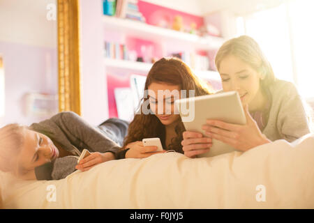 Les jeunes filles à l'aide de téléphones mobiles et tablettes numériques on bed Banque D'Images