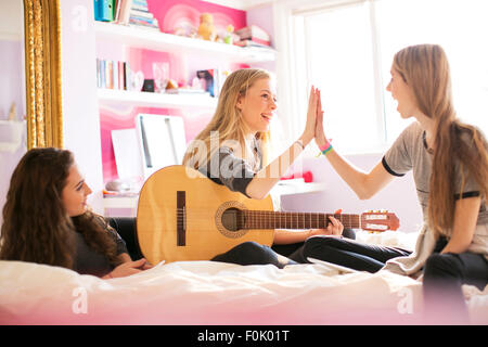 Les adolescentes avec guitare high fiving on bed Banque D'Images