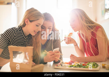 Teenage Girls eating sushi et texting with cell phone in cuisine ensoleillée Banque D'Images