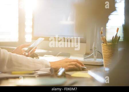 Woman using computer and texting on cell phone at desk Banque D'Images