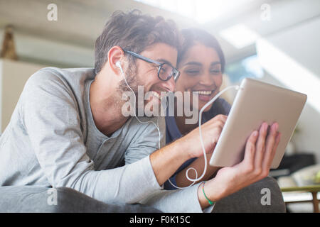 Smiling couple avec des écouteurs using digital tablet Banque D'Images