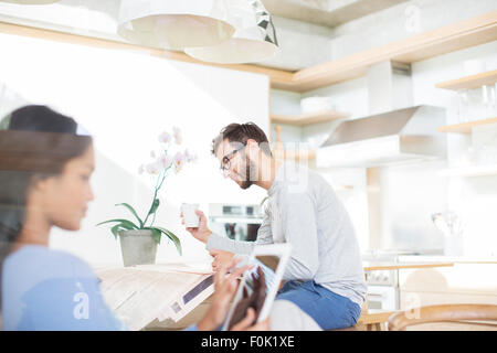 Couple de boire du café en lisant le journal, using digital tablet in kitchen Banque D'Images