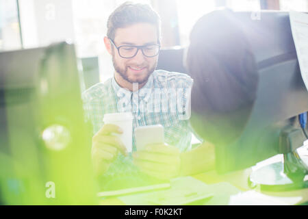 Creative businessman drinking coffee and texting with cell phone at computer Banque D'Images