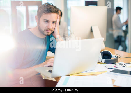 Creative sérieux businessman using laptop with head in hands Banque D'Images