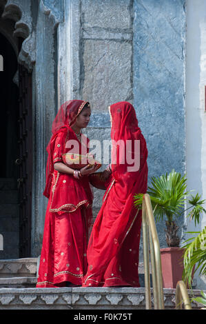 Udaipur, Inde. Deux femmes en saris rouges du Rajasthan à l'extérieur du palais de la ville. Banque D'Images