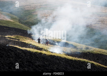 Herbes de gravure sur les Maures au-dessus de Glossop dans le Derbyshire. Les hommes de battre les fumeurs d'herbe. Une partie de la gestion de la lande. Banque D'Images