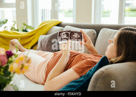 Pregnant woman looking at ultrasound scan tout en vous relaxant sur le canapé Banque D'Images