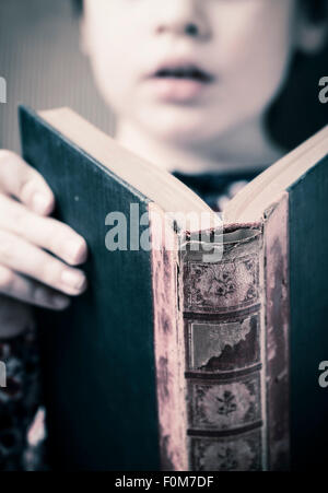 Petite fille dans un vieux livre de lecture. Image conceptuelle de l'intelligence et l'apprentissage de la lecture à un jeune âge. Banque D'Images