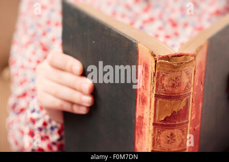 Petite fille en robe dans un vieux livre de lecture. Image conceptuelle d'apprendre à lire à un jeune âge. Banque D'Images