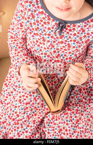 Petite fille dans un vieux livre de lecture. Image conceptuelle de l'intelligence et l'apprentissage de la lecture à un jeune âge. Banque D'Images