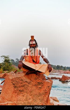 Sadhu hindou, ou saint homme, assis sur un rocher dans la rivière Betwa, Orchha, Madhya Pradesh, Inde Banque D'Images