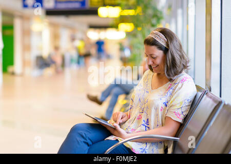 Jeune femme à l'aide d'une tablette numérique en zone d'attente de l'aéroport Banque D'Images