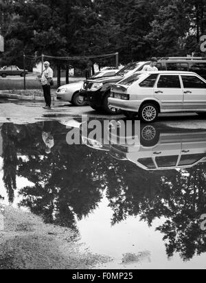 Après une forte pluie, verglas les voitures et les arbres se reflètent dans une flaque d'eau dans la route Banque D'Images