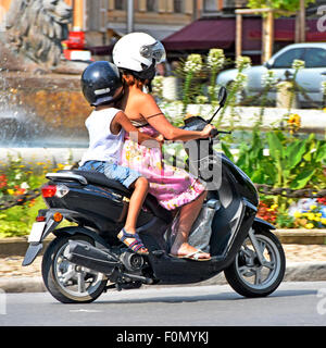 Femme scooter rider avec de jeunes petit enfant équitation leurs sur une chaude journée d'été à Aix en Provence (obscurci) plaque Banque D'Images