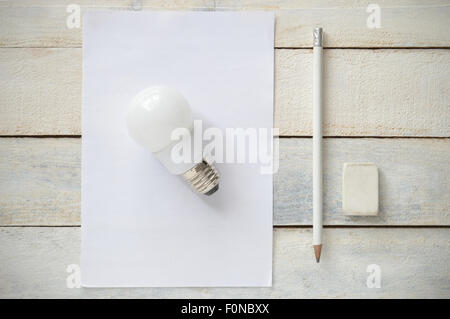 Droit d'inspiration représentant la simplicité d'une bonne idée. Une ampoule sur un papier blanc vide à côté d'une plume blanche et un caoutchouc. Banque D'Images