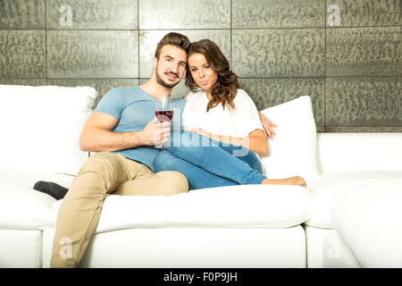 Un jeune couple dans le salon, buvant un verre de vin rouge sur le canapé. Banque D'Images