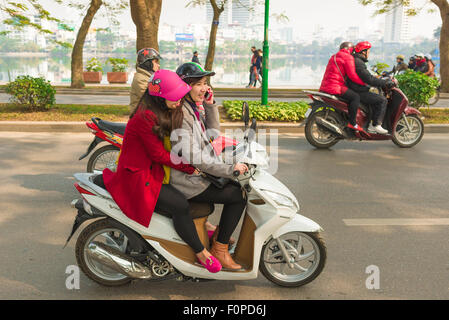 Amitié des amies féminines, vue de deux jeunes femmes conduisant une moto ensemble sur West Lake Causeway à Hanoi, Vietnam Banque D'Images