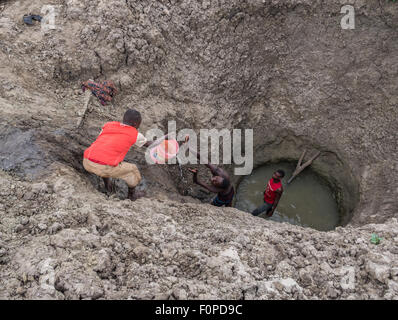 Les hommes obtenir de l'eau pour leur bétail d'un profond trou artificiel en Tanzanie, Afrique. Banque D'Images