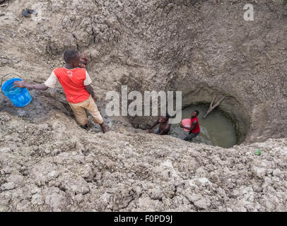 Les hommes obtenir de l'eau pour leur bétail d'un profond trou artificiel en Tanzanie, Afrique. Banque D'Images