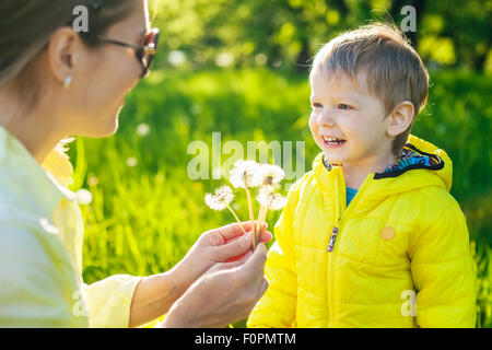 Mignon bébé garçon faisant un avec avant de sucer les pissenlits séchés dans mother's hands Banque D'Images