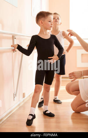 Les jeunes garçons travaillant à la barre dans une classe de danse de ballet. Réglage de la position de l'enseignant de l'un d'entre eux. Banque D'Images