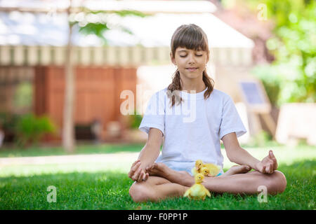 Petite fille se détendre tout en étant assis sur l'herbe, avec de petits canetons Banque D'Images