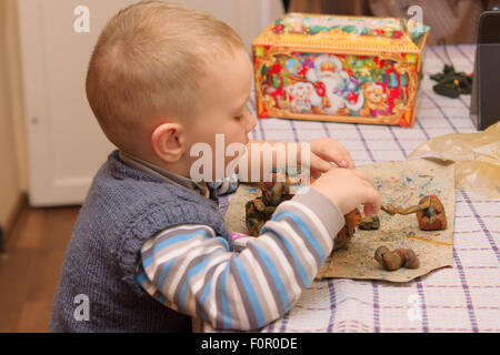 Le petit garçon est assis à une table et produits de moules de la pâte à modeler Banque D'Images