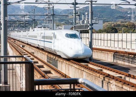 Le Japon, l'Shin-Tosu. Un blanc avec bande bleue à l'ouest du Japon Shinkansen, le train à grande vitesse, 700N series super express entrée en station sur des pistes. Banque D'Images