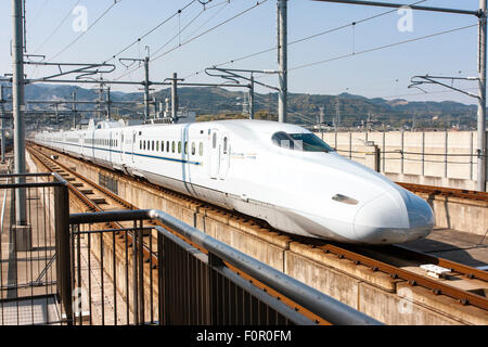 Le Japon, l'Shin-Tosu. Un blanc avec bande bleue à l'ouest du Japon Shinkansen, le train à grande vitesse, 700N series super express entrée en station sur des pistes. Banque D'Images