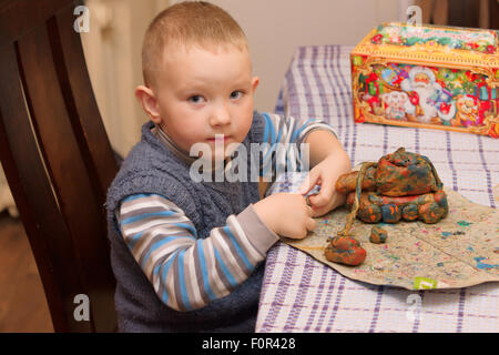 Le petit garçon est assis à une table et produits de moules de la pâte à modeler Banque D'Images