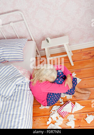 Pyjama rose avec femme triste et tissus assis sur le plancher à côté du lit Banque D'Images