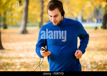 Jeune homme avec le casque d'exécution en nature de l'automne et à la recherche de téléphone mobile Banque D'Images