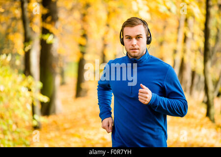 Jeune homme avec un casque jogging en automne nature et l'écoute de la musique Banque D'Images