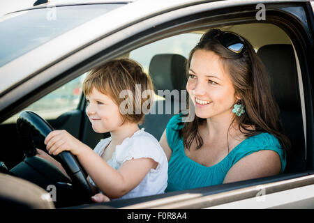 La mère et l'enfant prétendre driving car assis à la fois sur l'avant du siège conducteur Banque D'Images