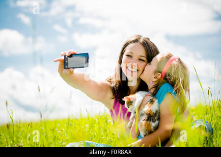 Jeune femme prenant des photos avec son smart-phone de la caméra elle-même, de sa fille et de chaton Banque D'Images